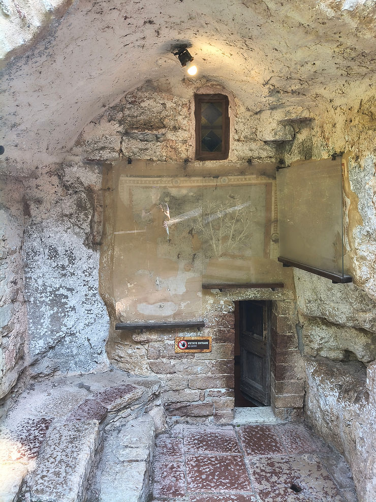 Rough stone cave chamber with a small door, lit bulb, and No Entry sign; old walls and tiled floor.
